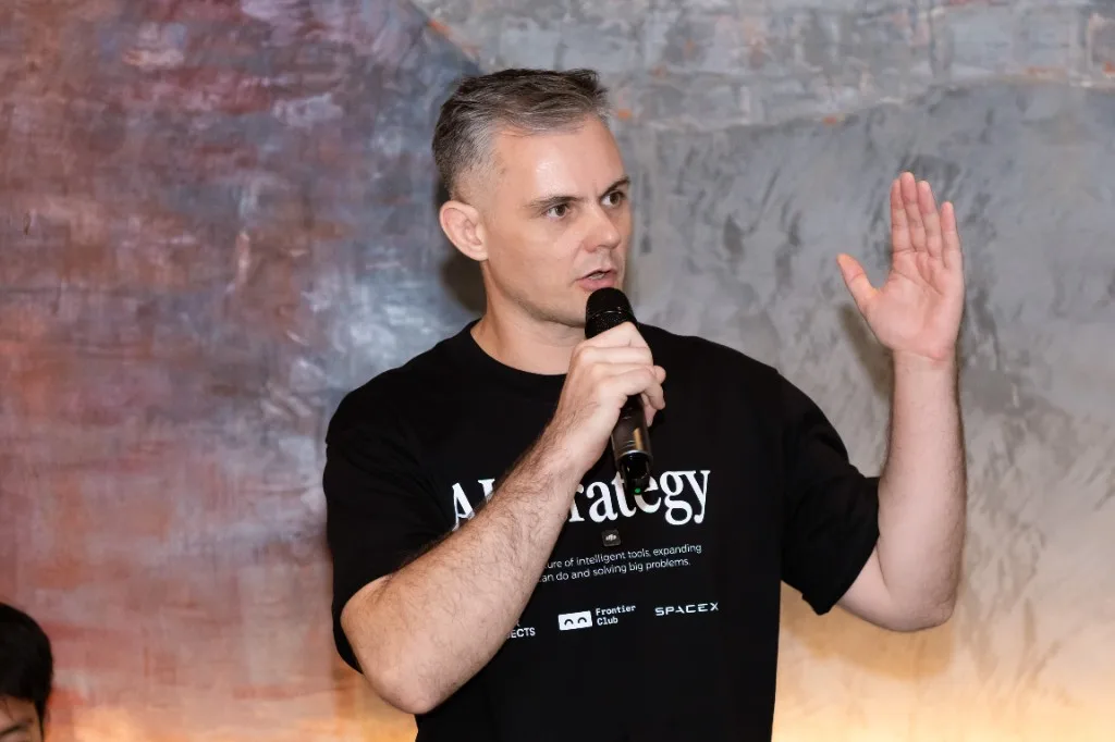 Speaking into a microphone at a workshop, one hand raised